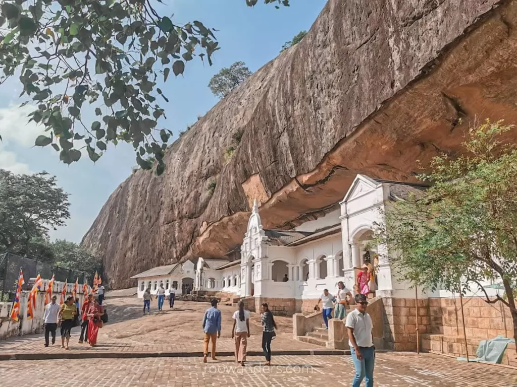 Visitors exploring the Dambulla Cave Temple beneath a massive rock in Sri Lanka.