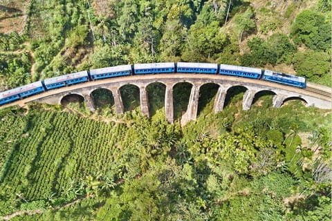 Aerial view of a blue train crossing the Nine Arch Bridge in Ella, Sri Lanka.