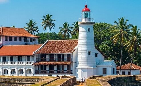 Historic Induruwa Lighthouse surrounded by colonial buildings and coconut palms.