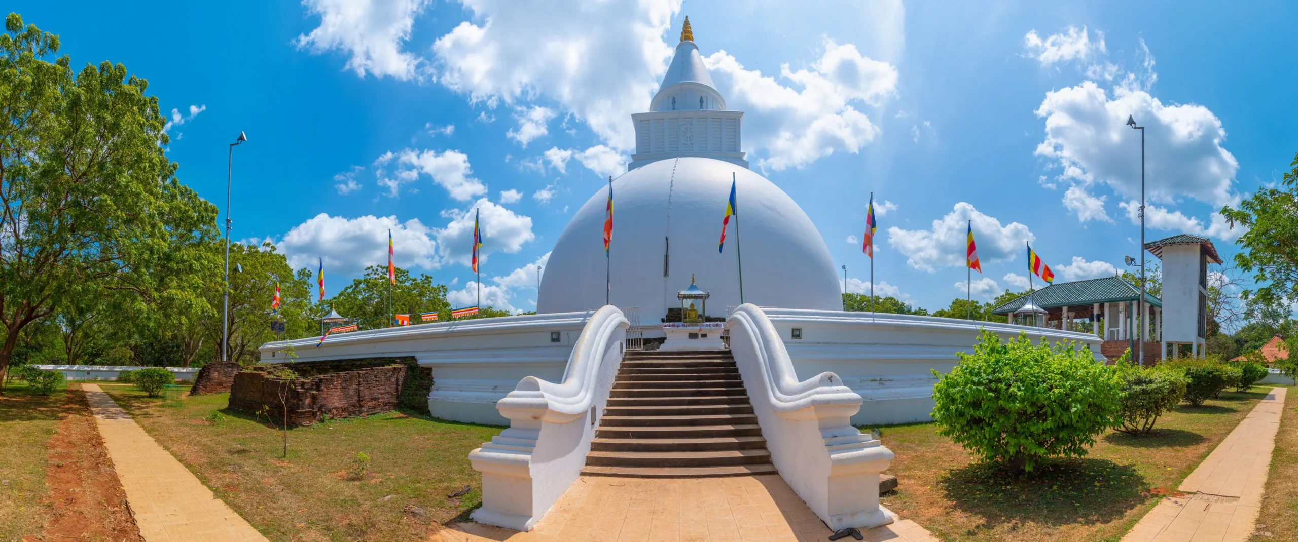 White Buddhist stupa surrounded by flags and gardens in Kataragama, Sri Lanka.
