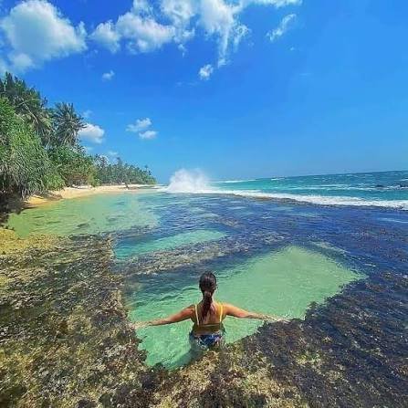 Traveller relaxing in a natural rock pool beside the ocean at Talpe Beach.