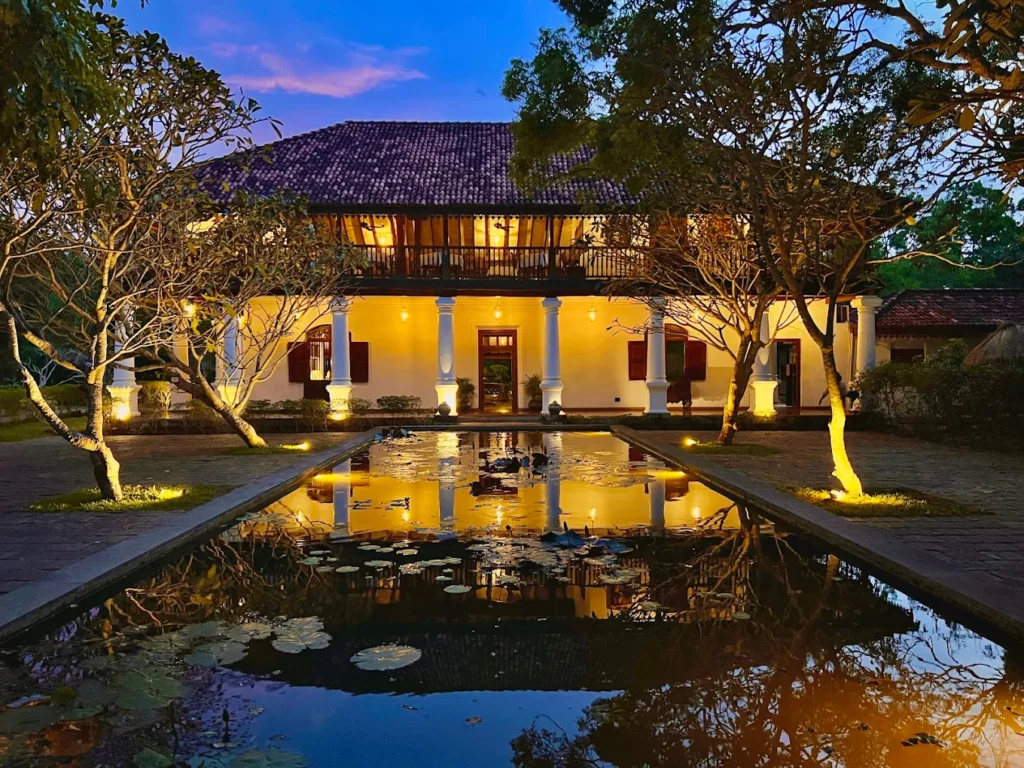 Uga Ulagalla’s restored heritage mansion illuminated beside a reflective lily pond.