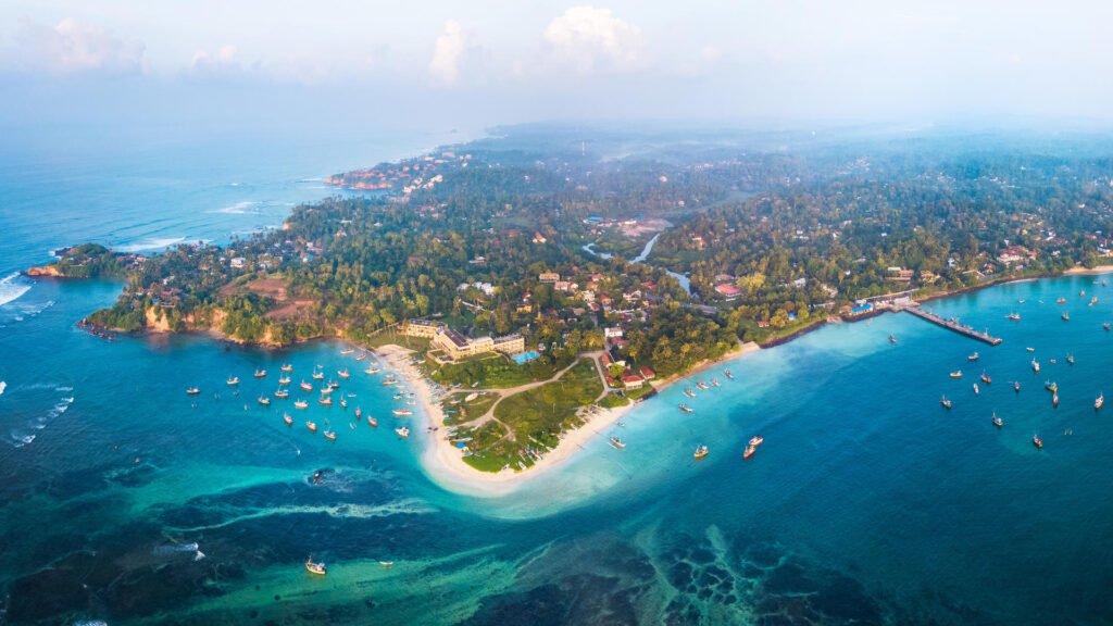 Aerial view of Weligama Beach with turquoise waters, fishing boats and a palm-lined coastline.