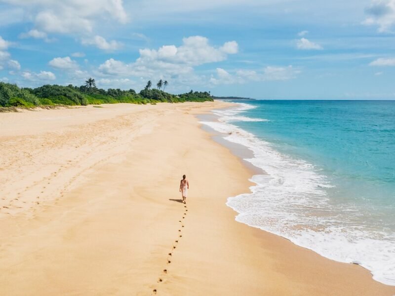 Traveller walking along a wide golden beach beside turquoise waters in Tangalle.