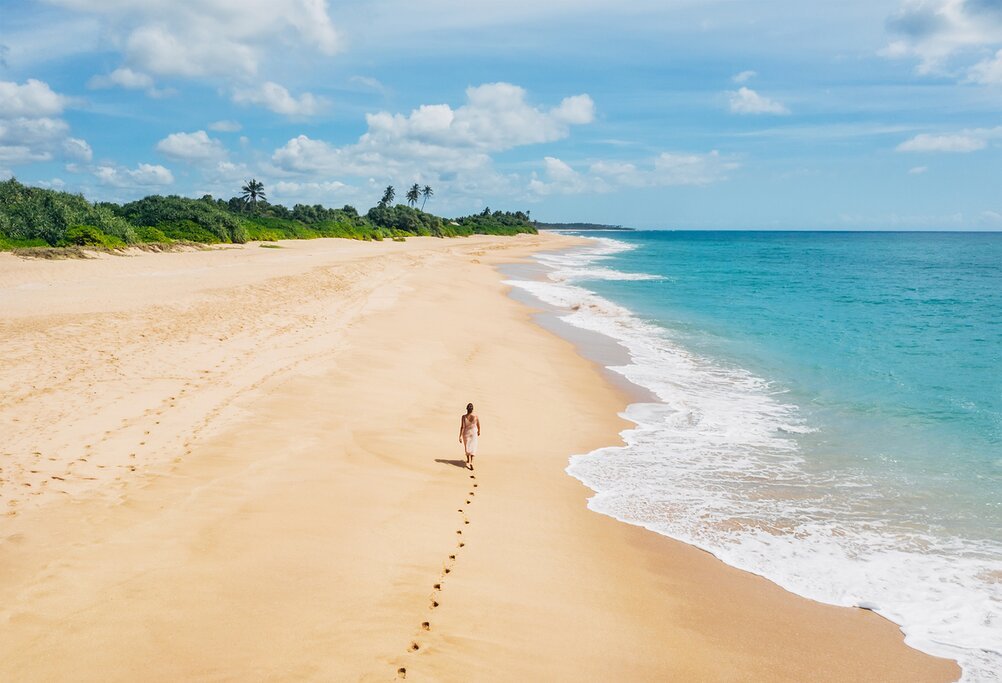 Traveller walking along a wide golden beach beside turquoise waters in Tangalle.