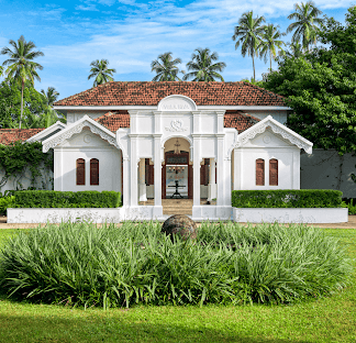 Colonial-style entrance of Uga Riva surrounded by tropical gardens.